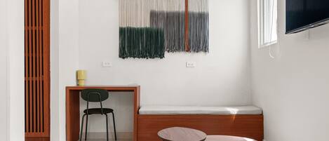 Una habitación pequeña y moderna con un escritorio de madera, una silla verde, un banco y una mesita.