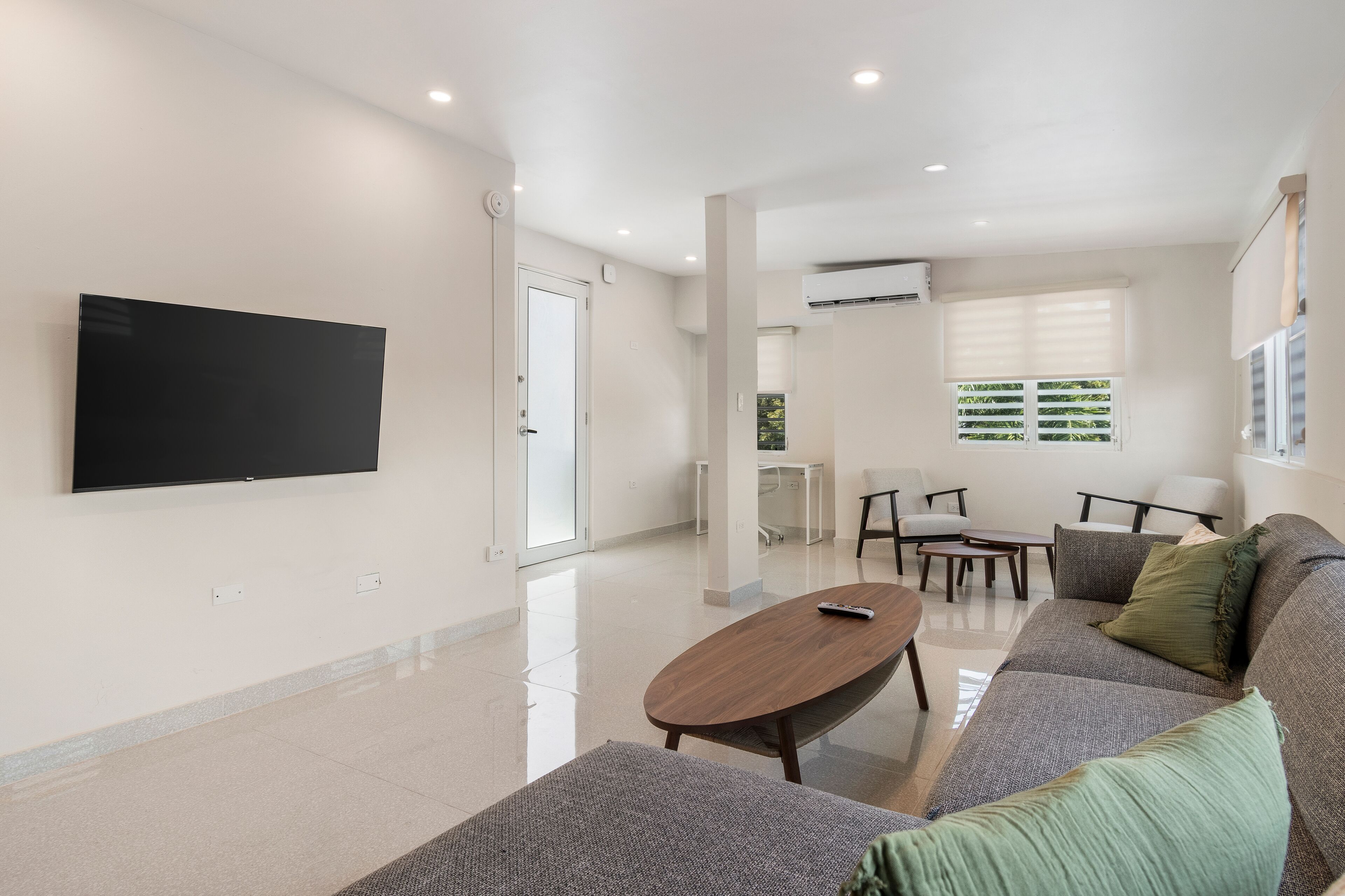 A modern living room with a flat-screen TV, a wooden coffee table, a grey sofa, and a dining area with chairs and a table.