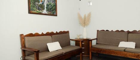 A room with two wooden sofas, a small table, a vase with pampas grass, and a painting on the wall.