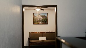 A room with a wooden bench, a ceiling fan, and a framed painting of a waterfall on the wall. - Hotel Cascada el Garruño (Calvillo)