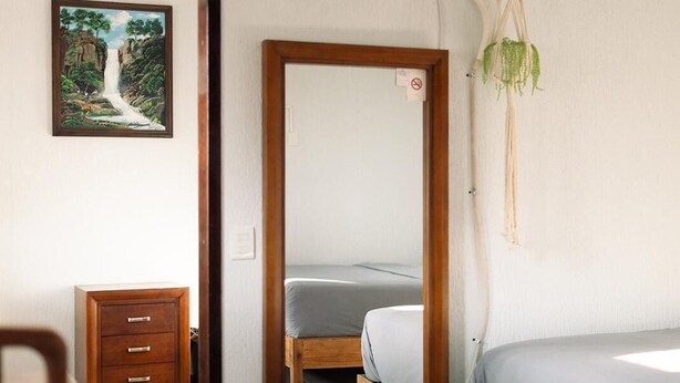 A bedroom with a wooden bed, a small bedside table, a chair, a mirror, and a picture on the wall. - Hotel Cascada el Garruño (Calvillo)