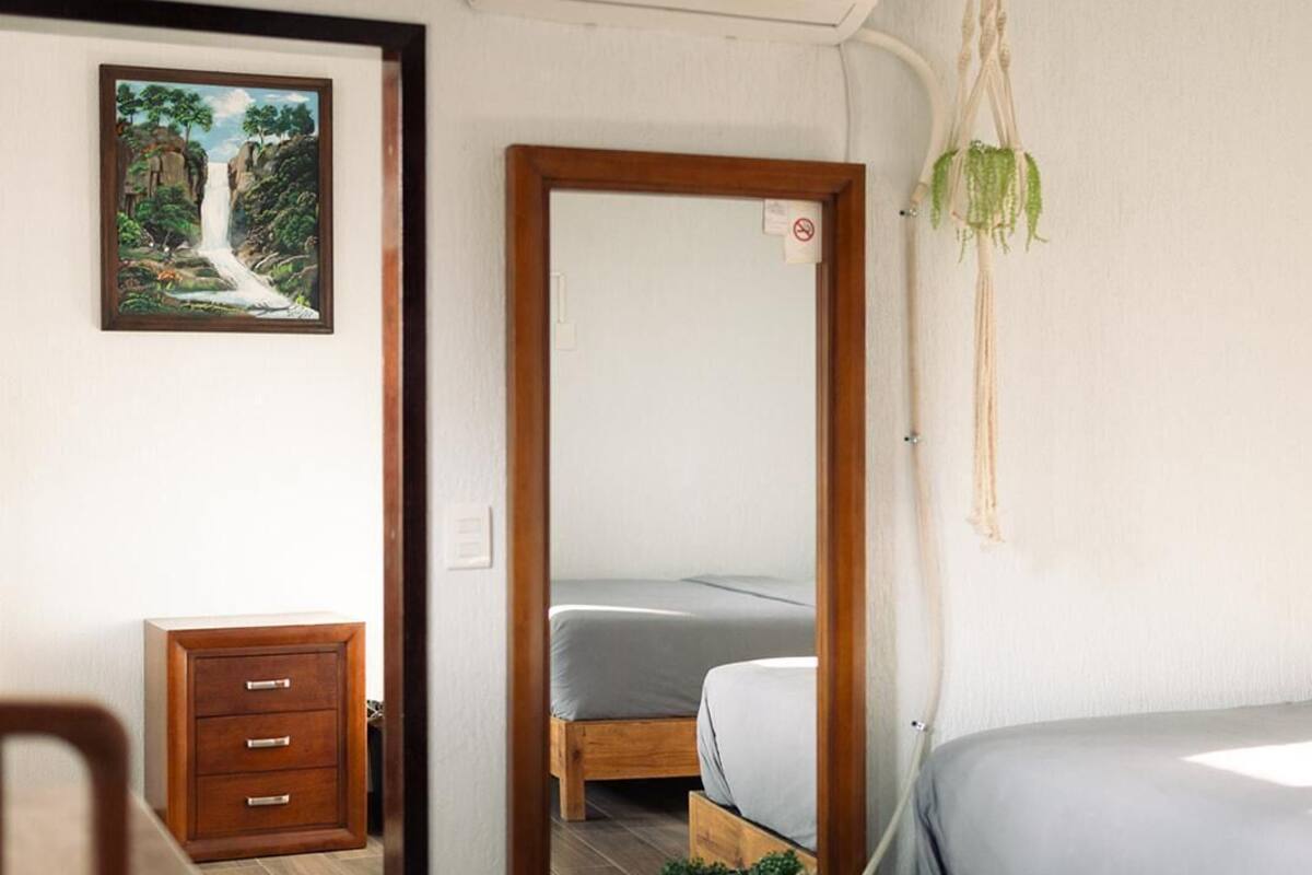 Un dormitorio con cama de madera, una mesita de noche pequeña, una silla, un espejo y un cuadro en la pared.