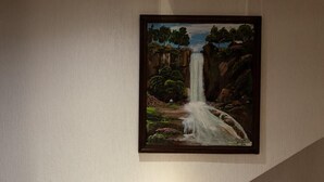 A dining area with a wooden chair and a framed painting of a waterfall on the wall. - Hotel Cascada el Garruño (Calvillo)