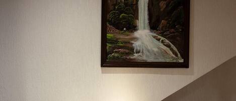 A dining area with a wooden chair and a framed painting of a waterfall on the wall.