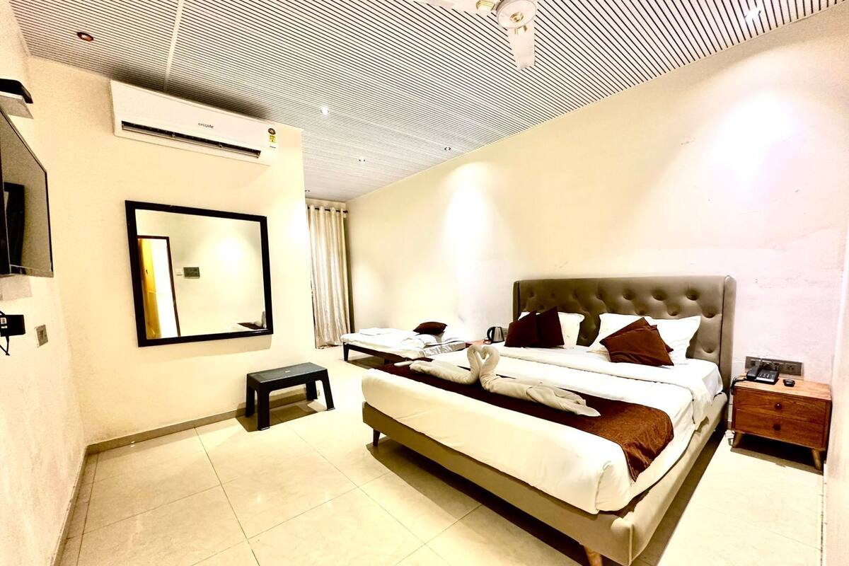 A hotel room with a bed, a bedside table, a mirror, and an air conditioning unit.
