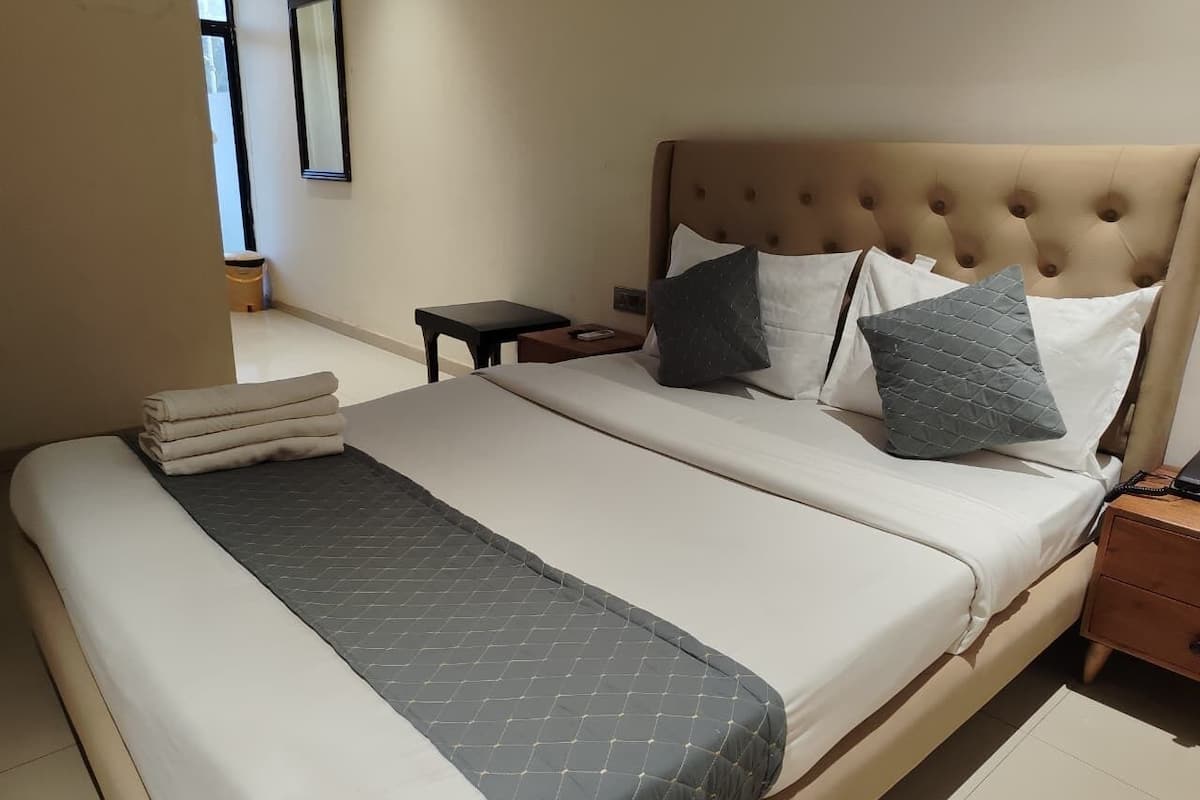 A double bed with a grey quilt, a wooden nightstand, a small table, and a mirror on the wall.
