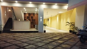 Amplo espaço interno com piso de azulejos, escada que leva a uma área de recepção e plantas em vasos.