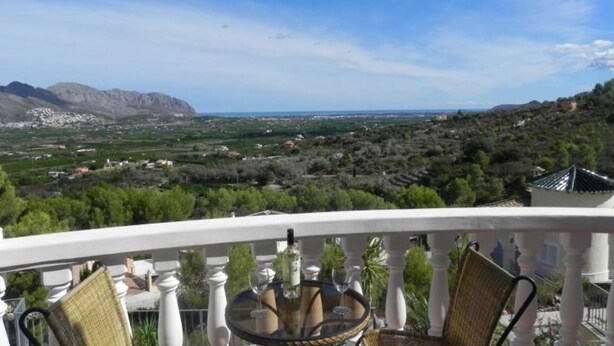 A balcony with a table and chairs, overlooking a mountainous landscape with a village below. - 6 Guests - Private Pool - 3Br Villa - Amazing View (Orba)