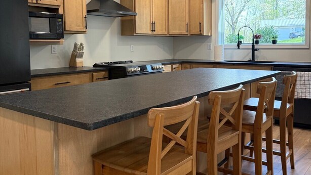 Una cocina moderna con armarios de madera, una isla grande con taburetes de bar, un microondas negro e iluminación colgante.
