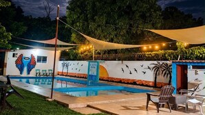 A swimming pool area with a mural, outdoor seating, and a night sky with clouds.