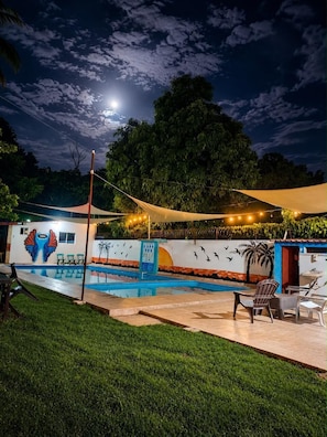 Un espace piscine agrémenté d’une fresque murale, de sièges extérieurs et d’une vue sur le ciel nocturne avec des nuages.