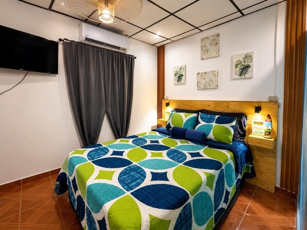 Een slaapkamer met een bed, gordijnen, een aan de muur hangend kunstwerk en een nachtkastje met een lamp.