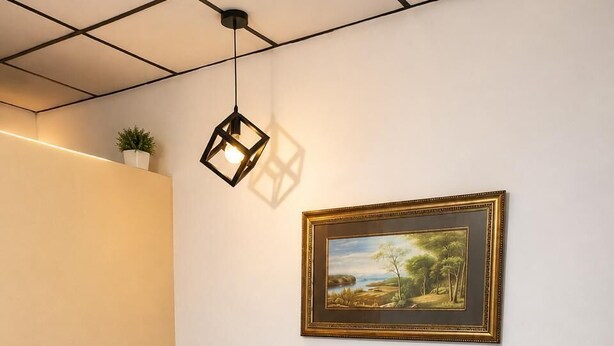 A single bed with a blue bedspread, a small potted plant on the wall, a framed landscape painting, and a geometric pendant light.