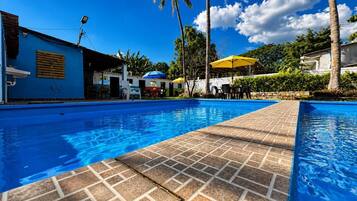 A swimming pool with a tiled deck, surrounded by palm trees and a clear blue sky.