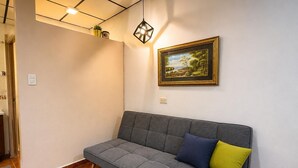 A room with a sofa, a framed picture on the wall, and a hanging light fixture.