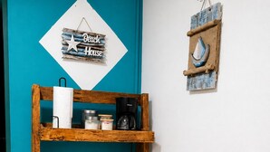 A wooden shelf unit with kitchenware and a sign reading 'Beach House' against a teal wall.