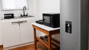 A compact kitchen with a stainless steel refrigerator, a microwave, and a sink with a faucet. There is a wooden table in front of the sink.