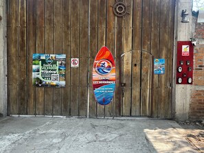 A wooden gate with a surfboard sign, a no parking sign, and a QR code for a surf magazine.