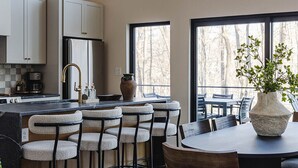 A modern kitchen with bar stools, a dining table, and large windows. - The Squire at Dunlap Ridge (Rockbridge)