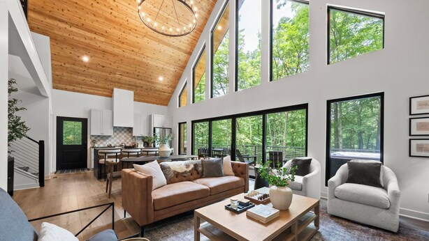 A spacious living room with a wooden ceiling, large windows, a sofa, a coffee table, and a dining area. - The Squire at Dunlap Ridge (Rockbridge)