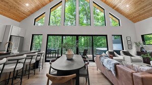 A spacious living area with a high ceiling and large windows, a dining area with bar stools, and a cozy seating area with a sofa and chairs. - The Squire at Dunlap Ridge (Rockbridge)