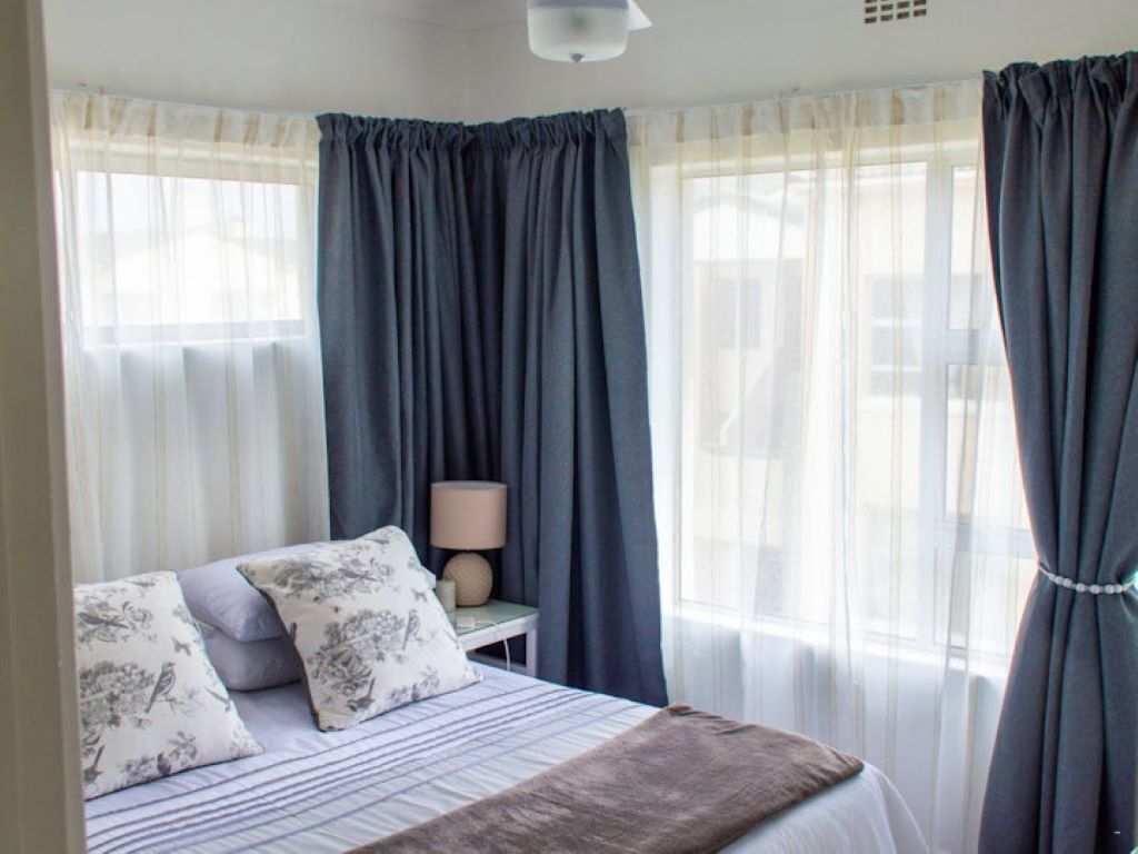 A bedroom with a bed, pillows, a bedside table with a lamp, and curtains.