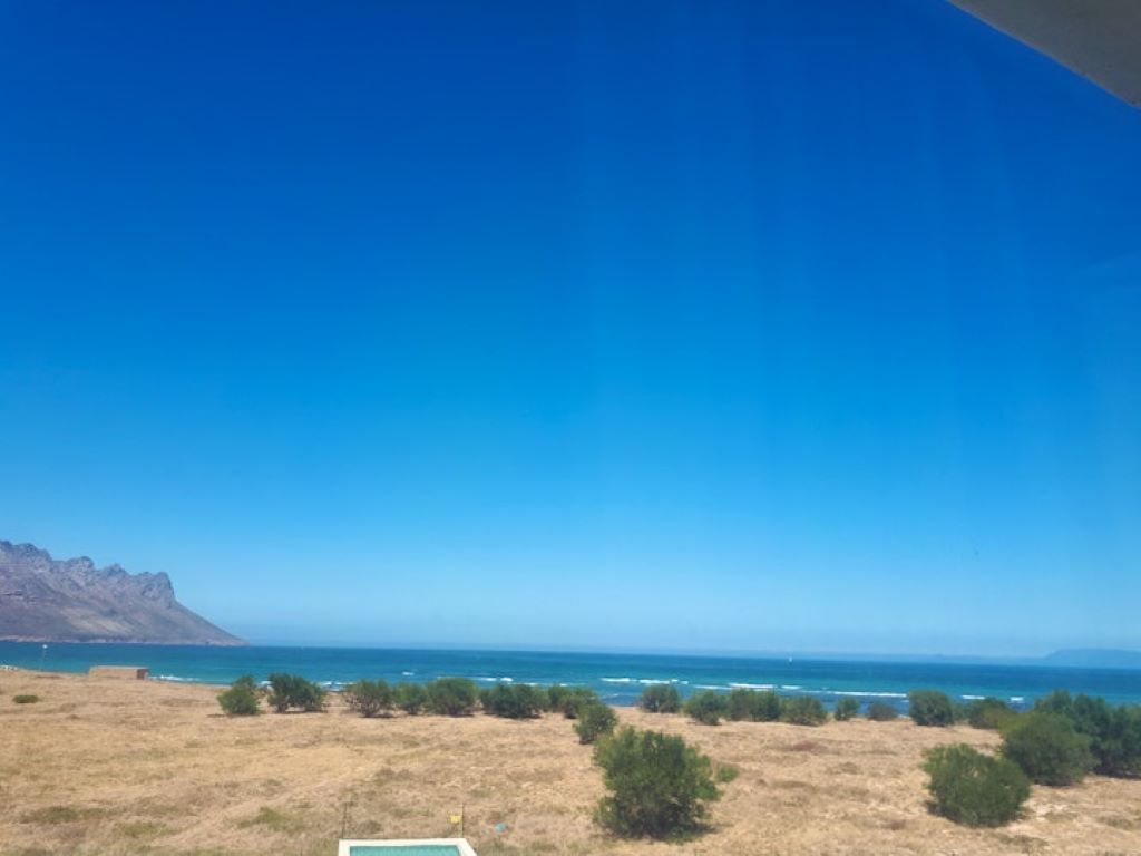 A coastal landscape with a clear sky, a view of the ocean, and sparse vegetation.
