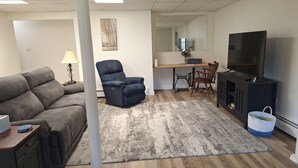 Een woonkamer met een bank, een relaxfauteuil, een televisie, een eettafel en een keukenhoek.