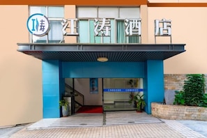 A hotel entrance with a blue awning, a signboard with hotel name, and a staircase leading inside.