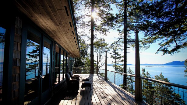 A wooden deck with outdoor seating, overlooking a body of water and forested area.
