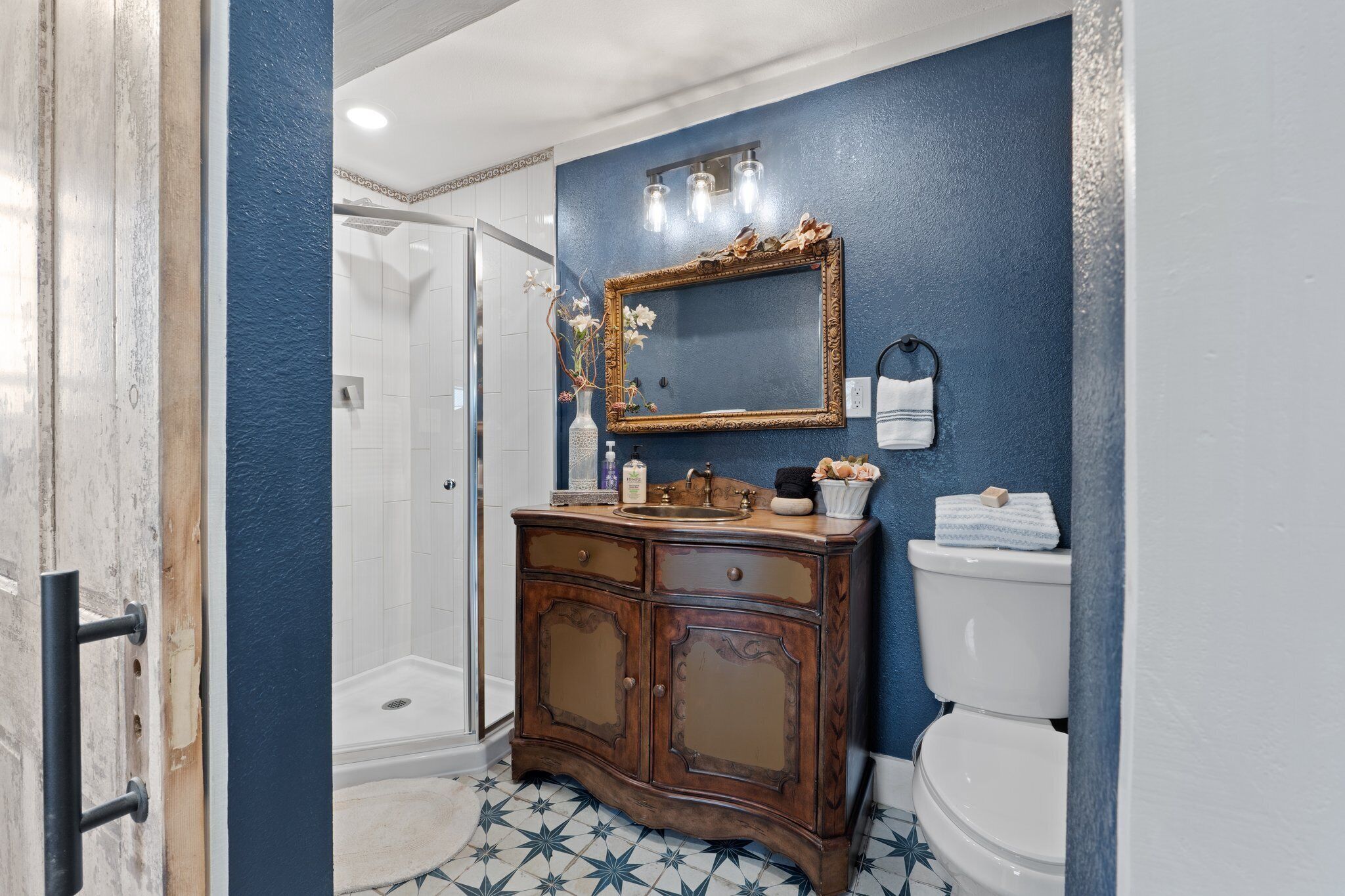 Ein Badezimmer mit blauer Wand, einem Holzwaschtisch, einer weißen Toilette und einer Duschkabine.