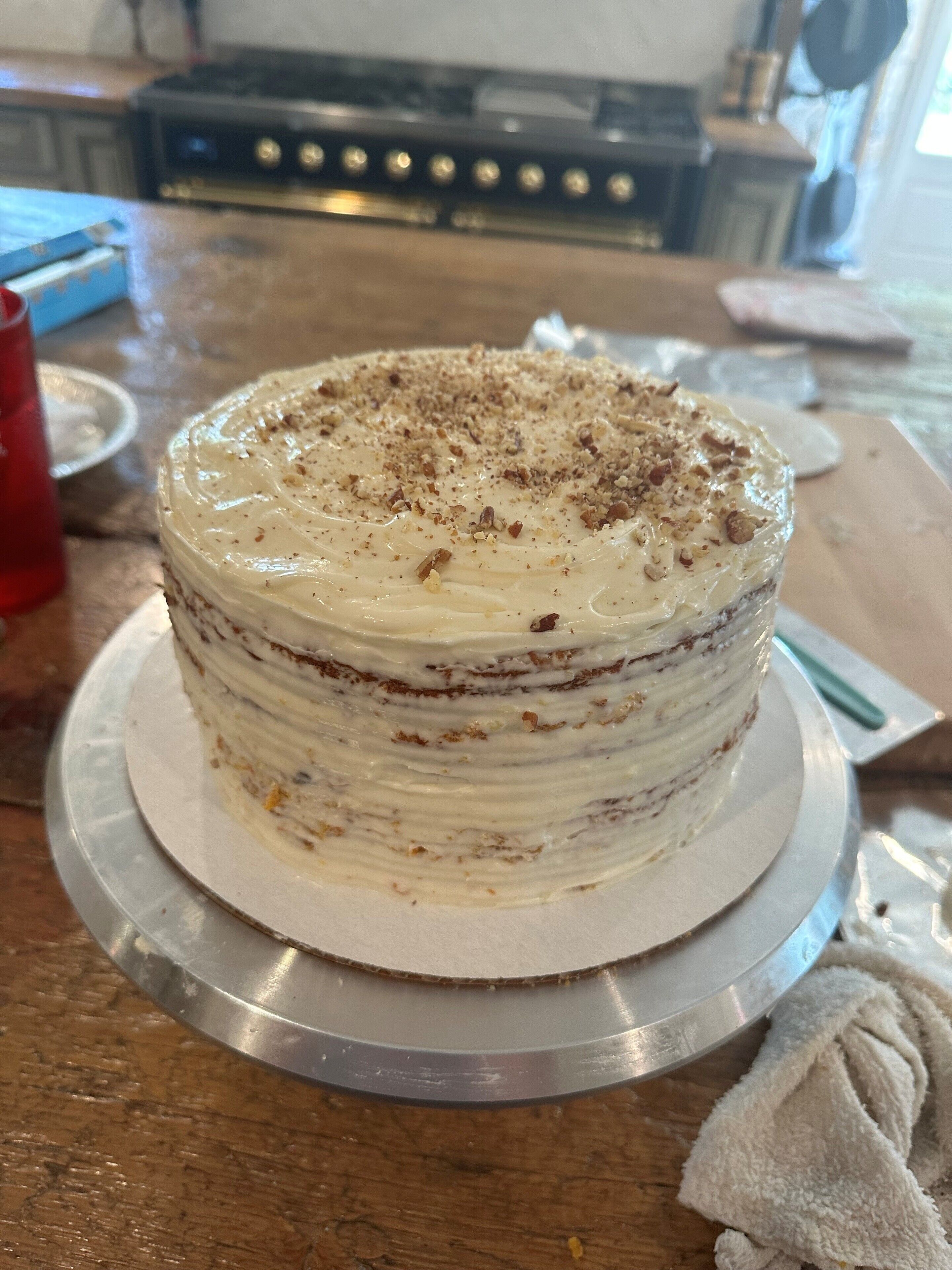 Un pastel de varias capas con cobertura blanca y nueces, sobre un soporte metálico.