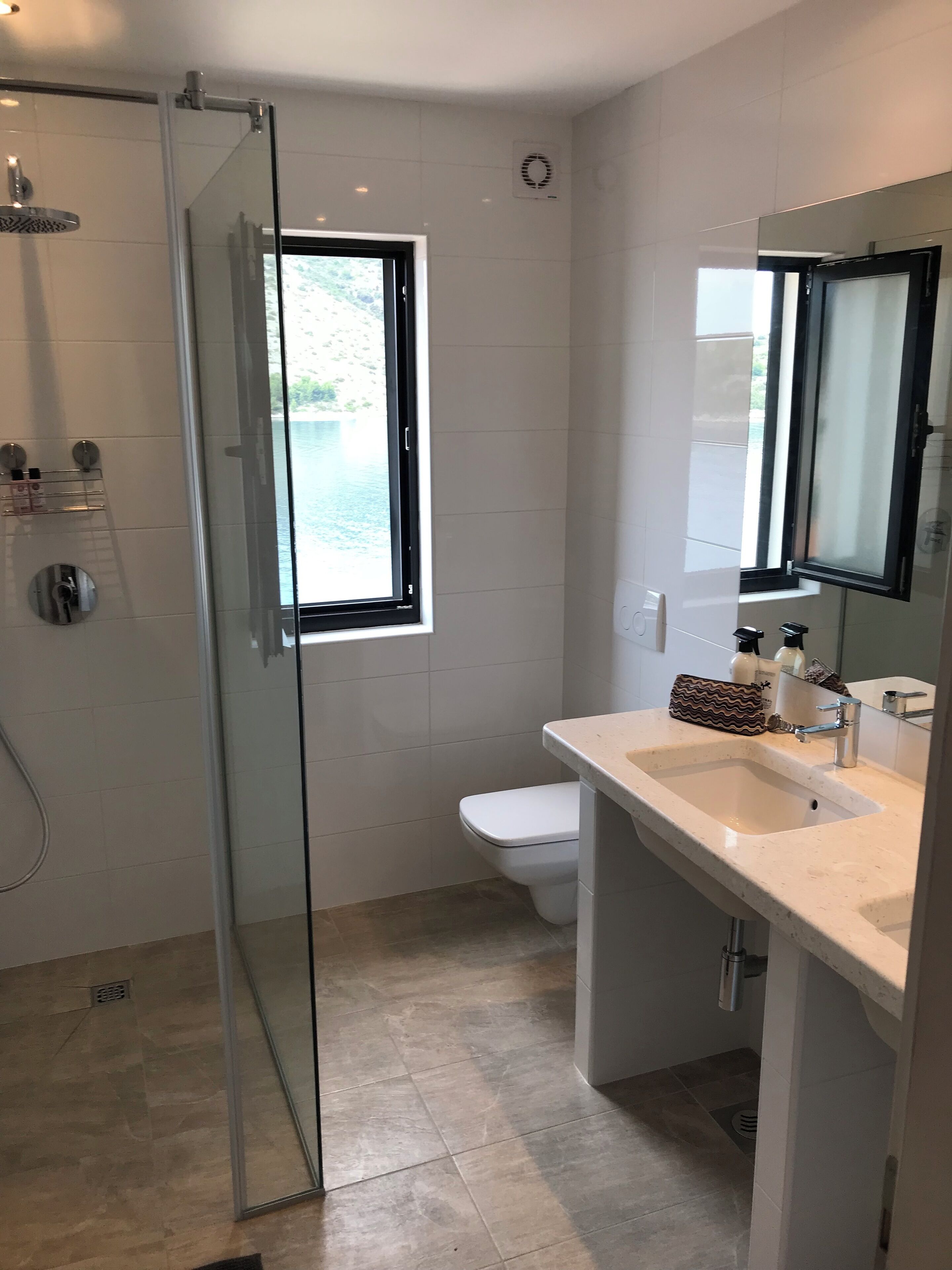 Un bany modern amb una dutxa de vidre, un vàter, un lavabo amb mirall i una finestra amb vistes a l'exterior.