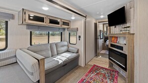 Interior compacto de una autocaravana con sofá, armarios integrados, televisor y una pequeña cocina.