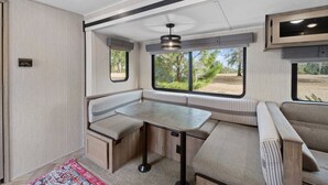 Interior compacto de una caravana recreativa, con kitchenette, zona de estar y ventanas amplias que ofrecen vistas del exterior.