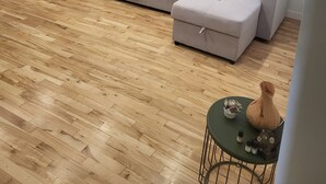 Ein modernes Wohnzimmer mit einem grauen Ecksofa, einem kleinen Schreibtisch mit Stuhl und einem runden Tisch mit Vase und Kerzen.