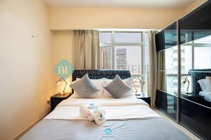 Camera d'albergo con un letto, cuscini, comodino, lampada e vista sugli edifici dalla finestra.