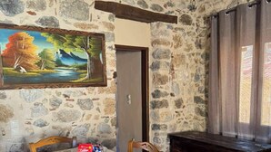 A dining area with a stone wall, a painting, a table with a white tablecloth, wooden chairs, and a bench. - Fani's house (Platanos)