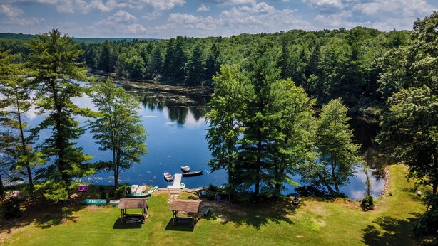 A lakeside property with a grassy area, a small dock, and boats. - 14-bedroom resort in tranquil Paupack. 1885 Farm & Guest House with Game Room! (Paupack)