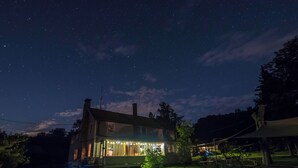 A house with a large windowed porch, a well-maintained lawn, and a clear night sky. - 14-bedroom resort in tranquil Paupack. 1885 Farm & Guest House with Game Room! (Paupack)