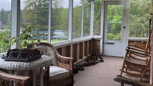 A covered porch with wicker furniture, a table with potted plants, and a view of a wooded area. - 14-bedroom resort in tranquil Paupack. 1885 Farm & Guest House with Game Room! (Paupack)