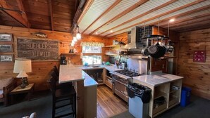 A rustic kitchen with wooden walls, a central island, and a stove. - 14-bedroom resort in tranquil Paupack. 1885 Farm & Guest House with Game Room! (Paupack)