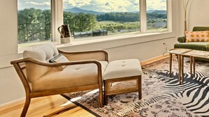 Une pièce avec une grande fenêtre, un canapé, une petite table et un fauteuil vert.