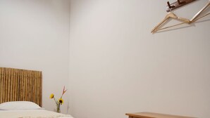 A bedroom with a bed, a wooden stool, a small table, and a wall-mounted hanger. - Muyuterra (Moyobamba)