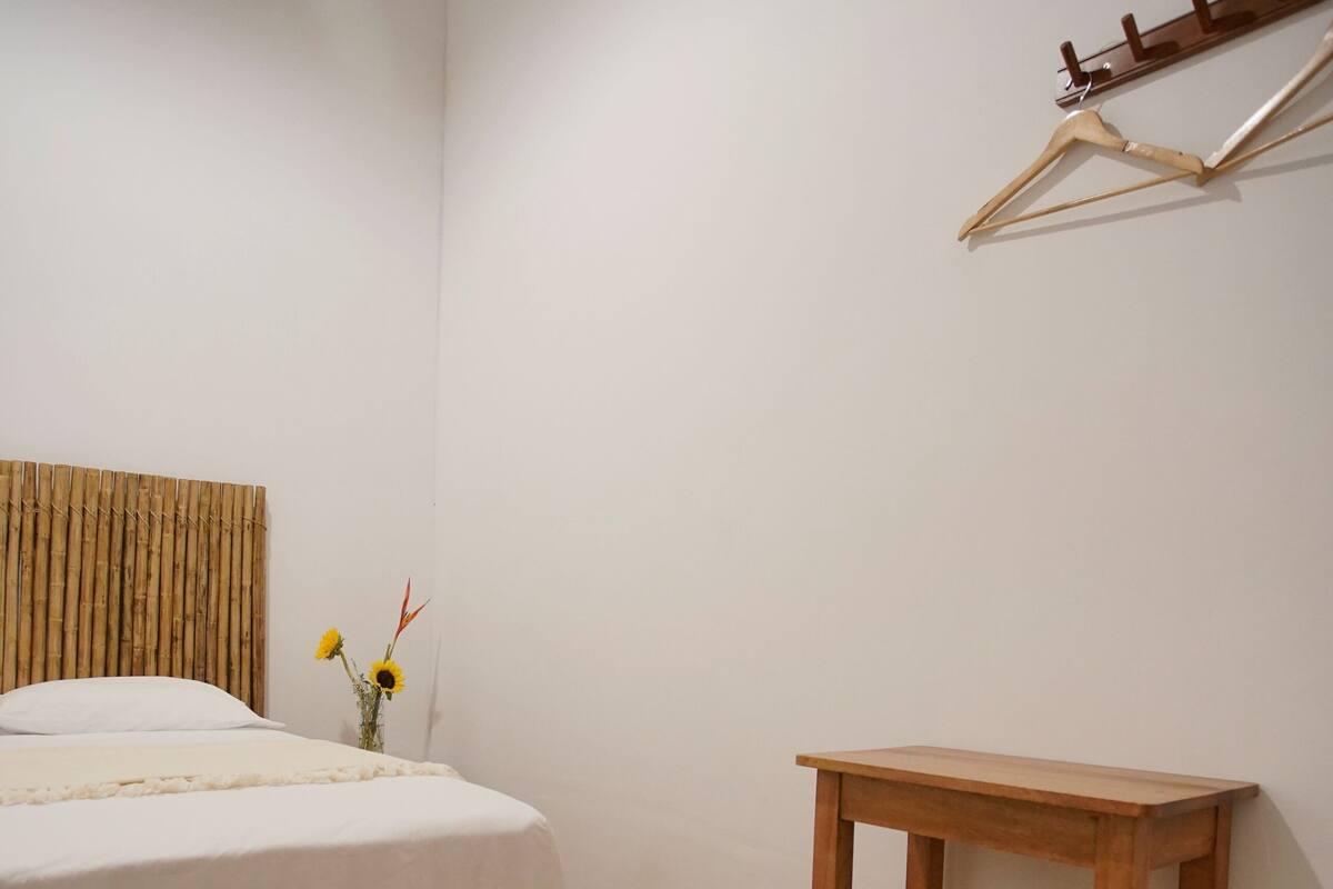 Une chambre à coucher comprenant un lit, un tabouret en bois, une petite table et un porte-manteau fixé au mur.