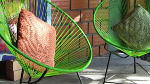 Two green wire-framed chairs with cushions, positioned in front of a brick wall with a mural. - Muyuterra (Moyobamba)