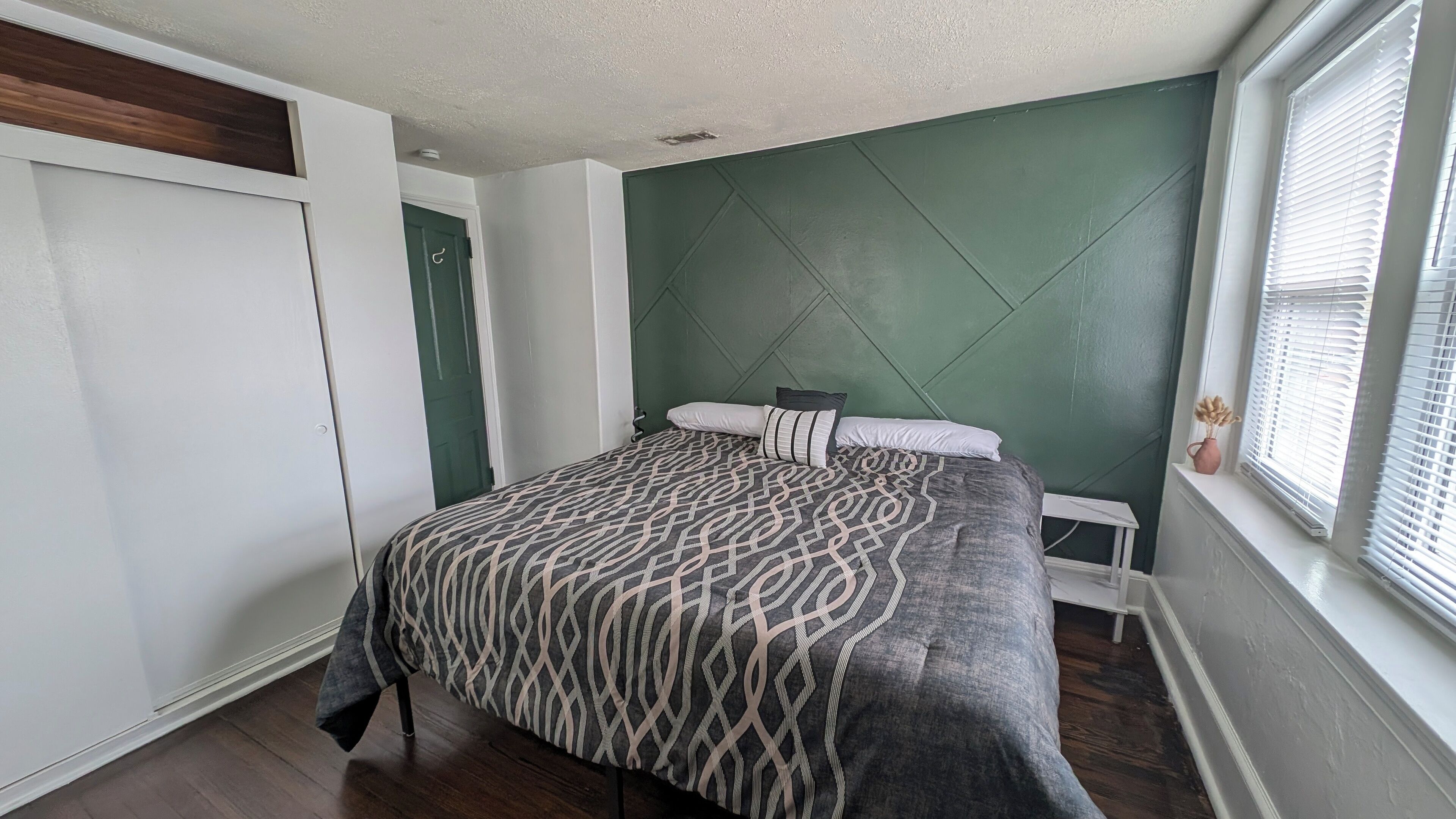 Une chambre à coucher avec un lit, une commode, une fenêtre avec des stores et une porte.