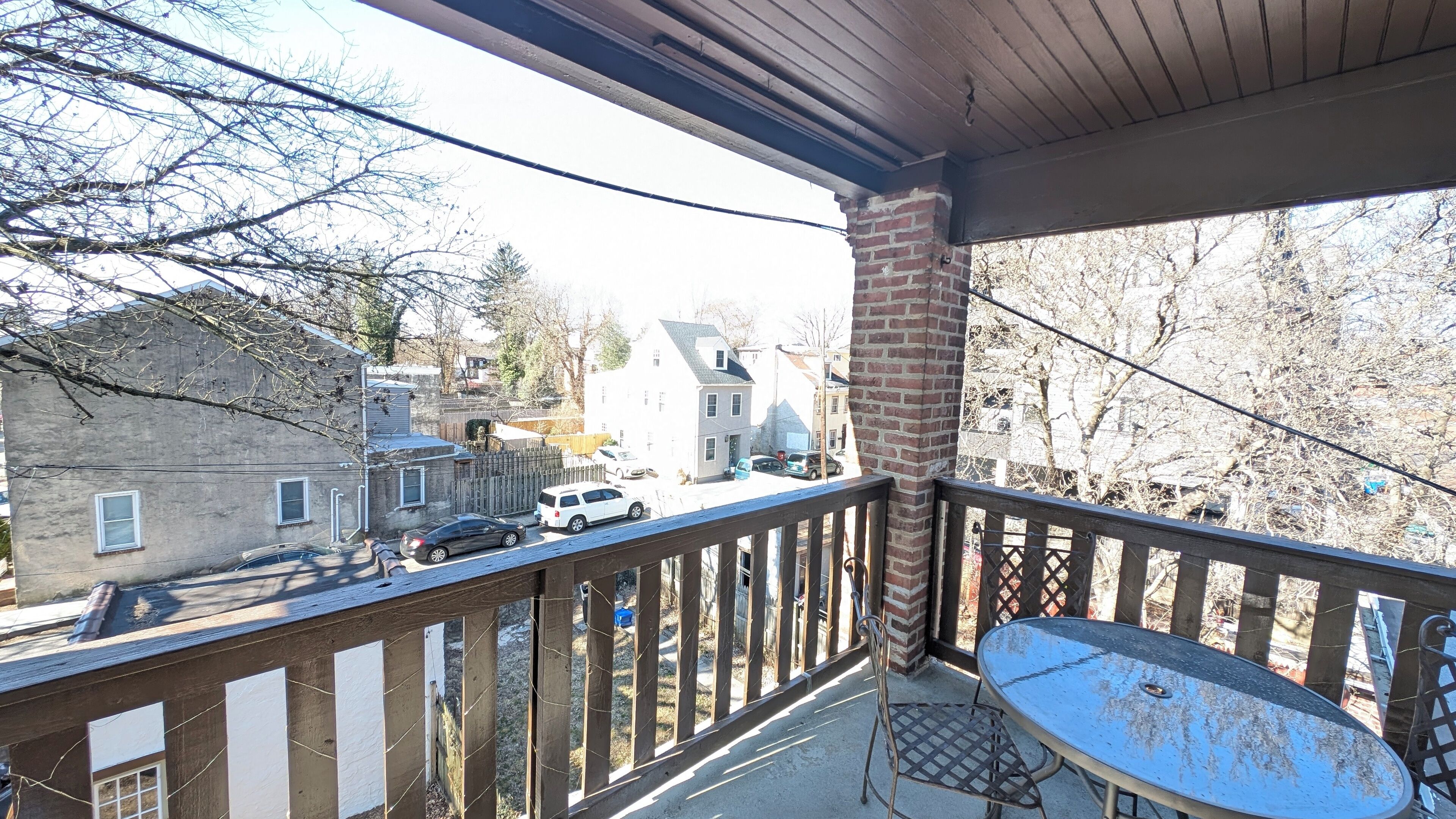 Ein Balkon mit Metalltisch und Stühlen, der auf eine Straße mit geparkten Autos und Häusern blickt.