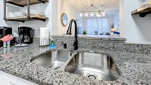 Eine Küche mit Granit Arbeitsplatten, einer Edelstahl-Spüle und einer Kaffeemaschine.