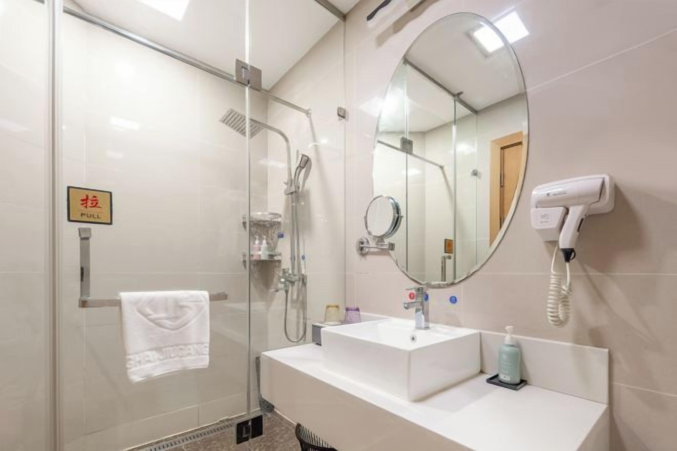 Een moderne badkamer met een douchecabine van glas, een witte wastafel, een spiegel en een haardroger bevestigd aan de muur.